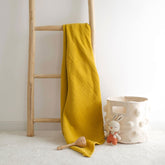 Mustard 4-ply organic muslin baby blanket hanging on ladder next to toy basket